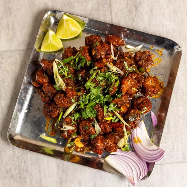 Pista House's Indian chicken kababs, garnished with cilantro, onions, and lime wedges on a silver tray.