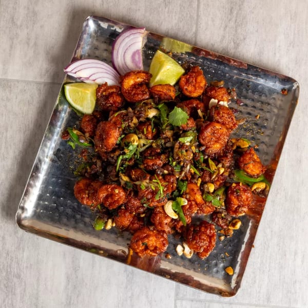 Pista House's Indian-style fried shrimp with cashews, onions, and lime wedges on a metal tray.