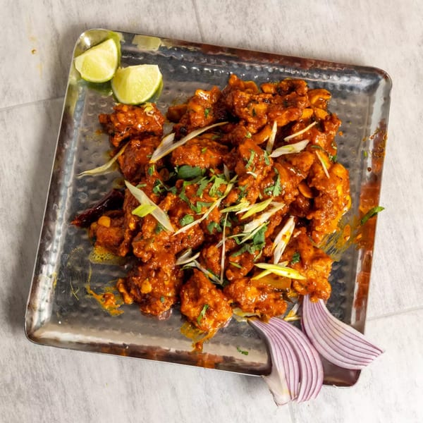 Pista House's Indian chicken dish, garnished with lime wedges, red onion, and green onions.