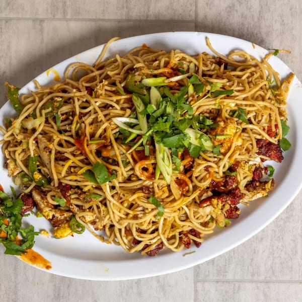 A large white platter of Pista House noodles with chicken, vegetables, and fresh herbs.