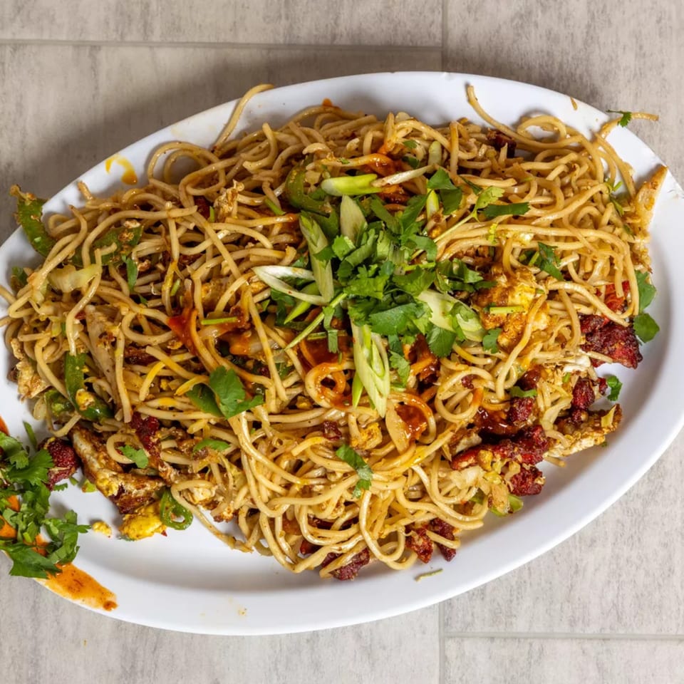 A large white platter of Pista House noodles with chicken, vegetables, and fresh herbs.
