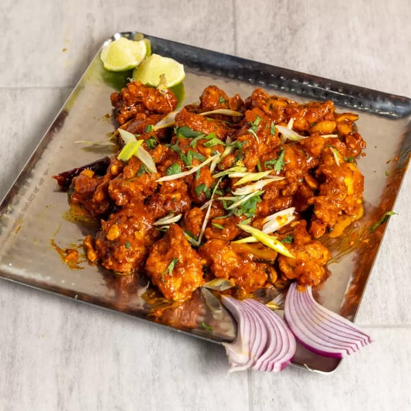 Pista House's Chicken 65, a spicy Indian appetizer, garnished with lime, cilantro, and red onion.