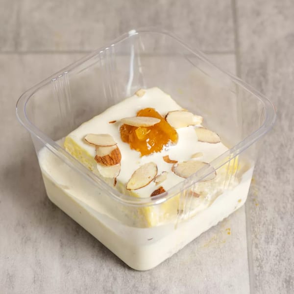 Pista House's Indian dessert, a square of white cake with cream, almonds, and orange jam in a plastic container.