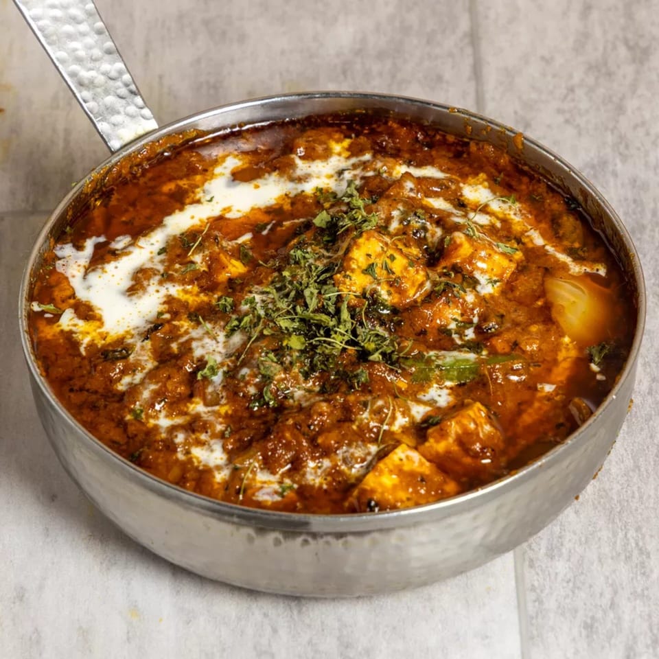 Pista House's paneer butter masala, a rich Indian curry with paneer, cream, and herbs in a metal pan.