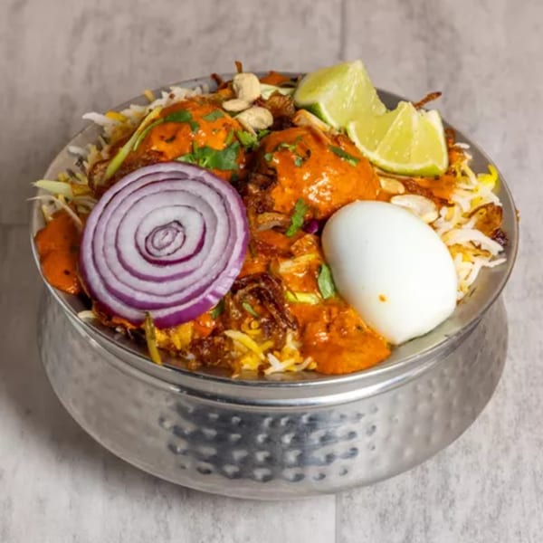Pista House Chicken Biryani with red onion, lime, cashews, and a boiled egg in a metal bowl.