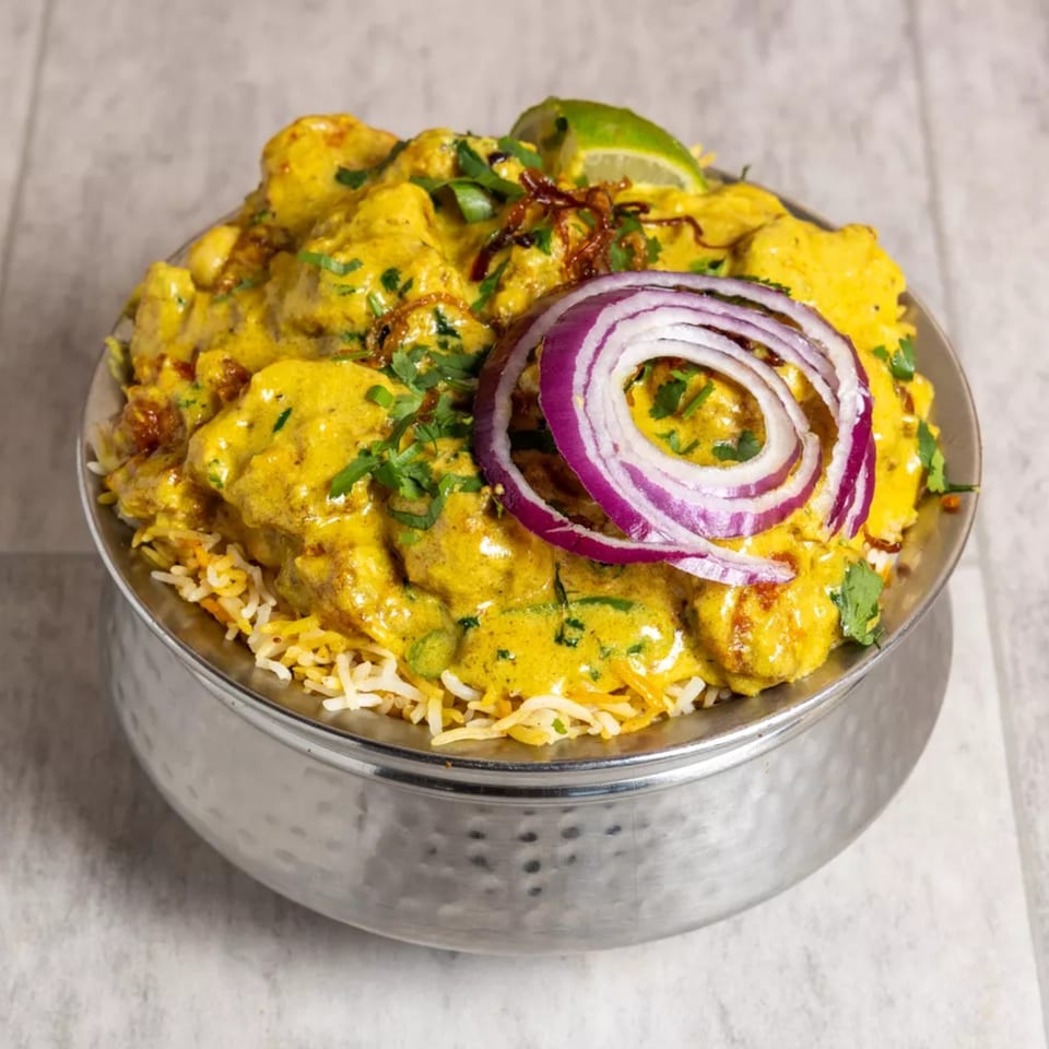 Pista House's Indian chicken biryani, topped with red onion, cilantro, and a lime wedge.