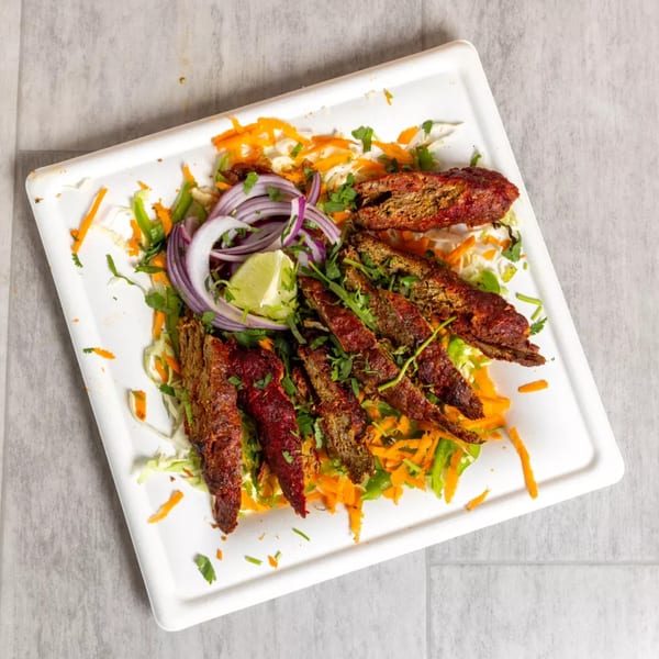 Pista House's Indian kababs, garnished with fresh onions, lime, and cilantro, on a white platter.