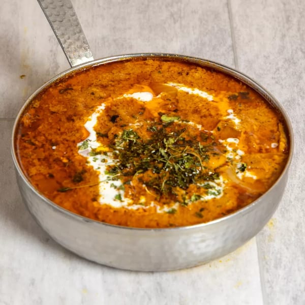 Pista House's Indian curry, a rich orange dish with cream swirls and green herbs in a metal pan.