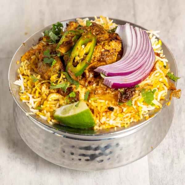 Pista House chicken biryani with green chilies, red onion, and lime in a steel bowl.